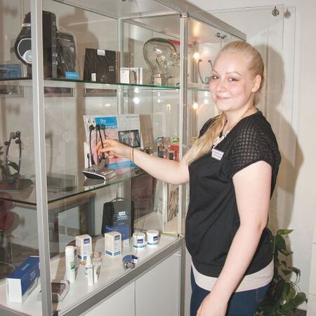 Junge Frau präsentiert Kosmetikprodukte in einer modernen Glasvitrine einer Apotheke.